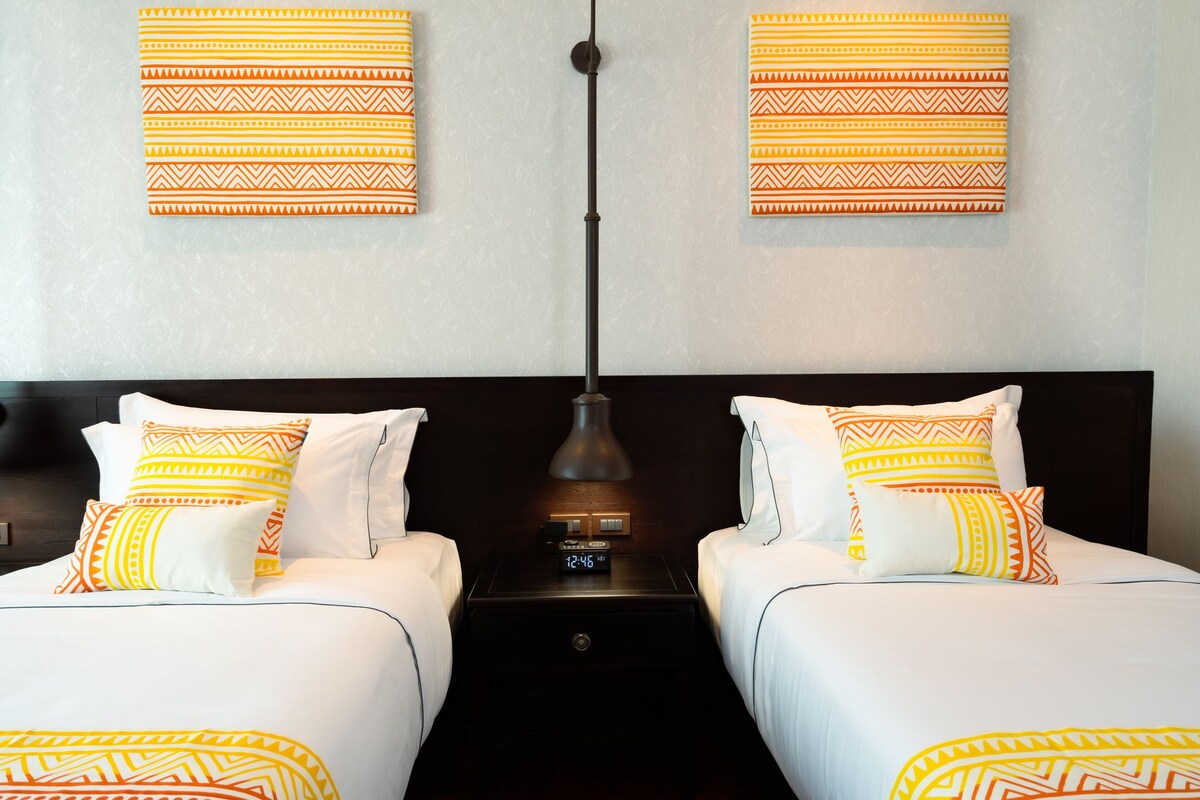 Una habitación de hotel con dos camas, una mesita de noche con un reloj y adornos decorativos en la pared.