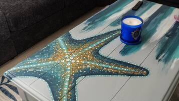 Una habitación con un sofá gris oscuro, una mesita de centro con un diseño de estrella de mar pintada y un candelabro azul.