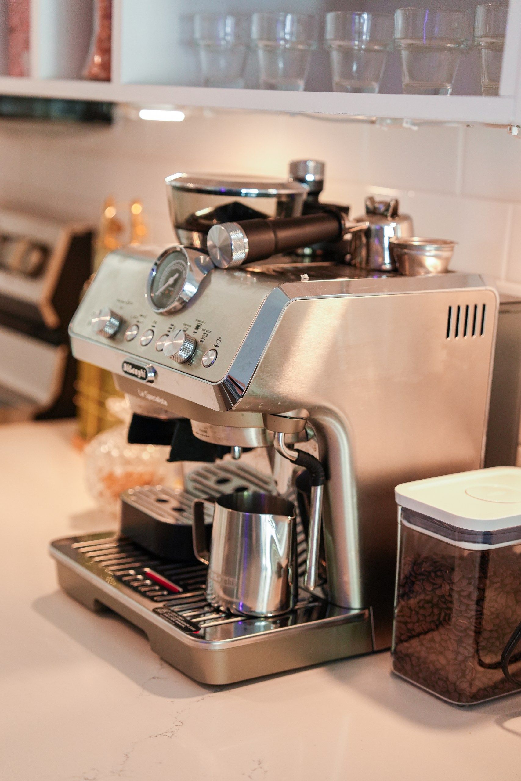 Una cafetera con un portafiltro, un espumador de leche y un recipiente con granos de café.
