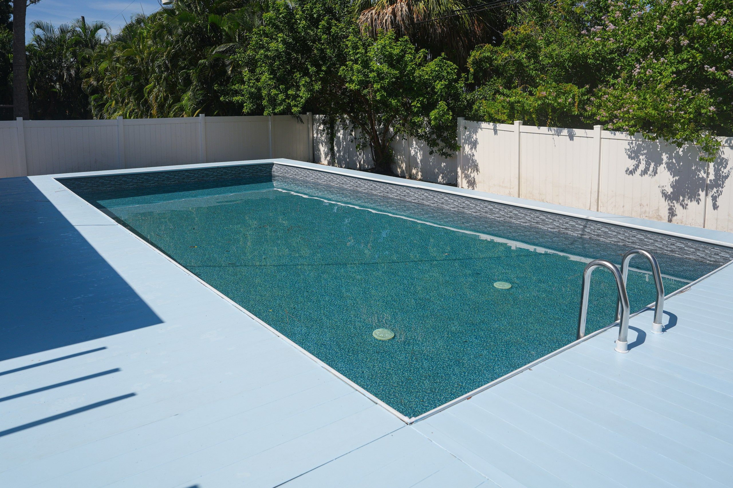 Una piscina rectangular con agua azul cristalina, rodeada por un solárium blanco y un muro bajo.