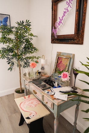 A room with a desk, a potted plant, a framed picture, and a neon sign.