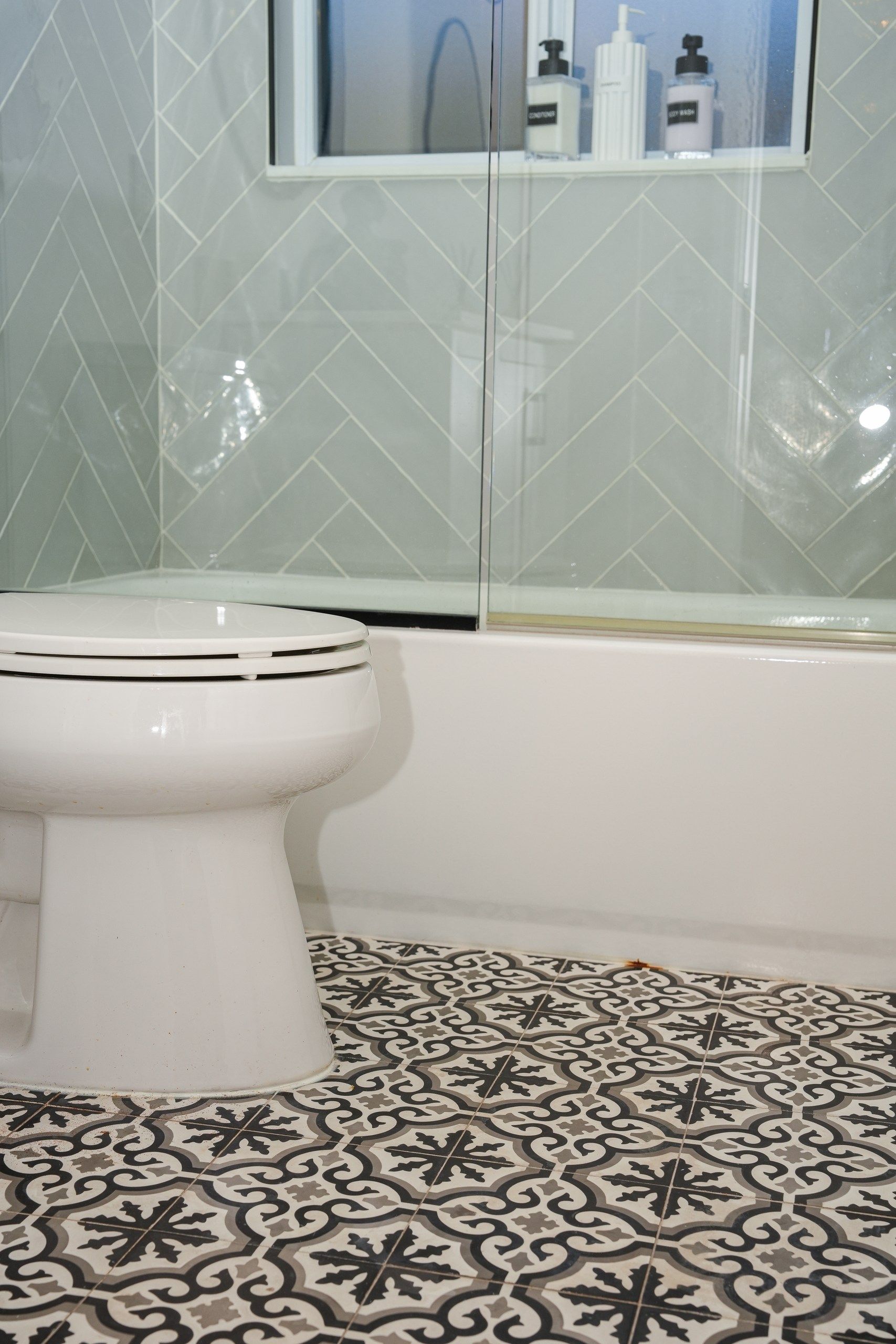 A bathroom with a white toilet, a glass shower enclosure, and patterned floor tiles.