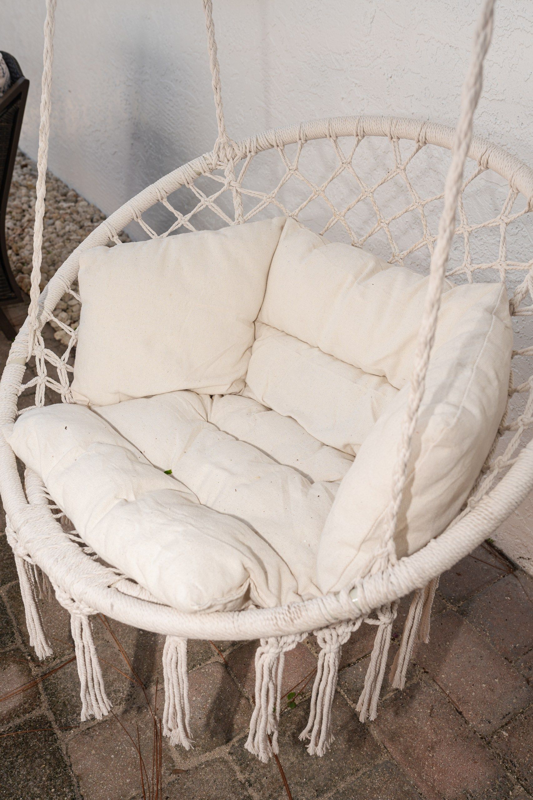 A white macrame hanging chair with cushions.