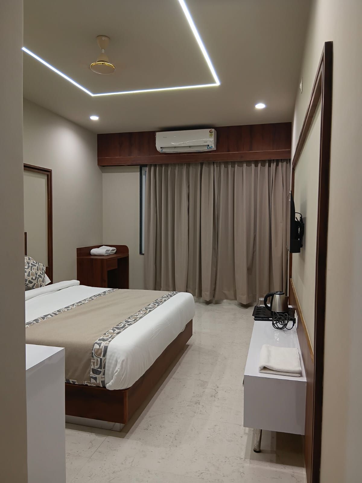 A hotel room with a bed, bedside table, air conditioning unit, and a mirror.