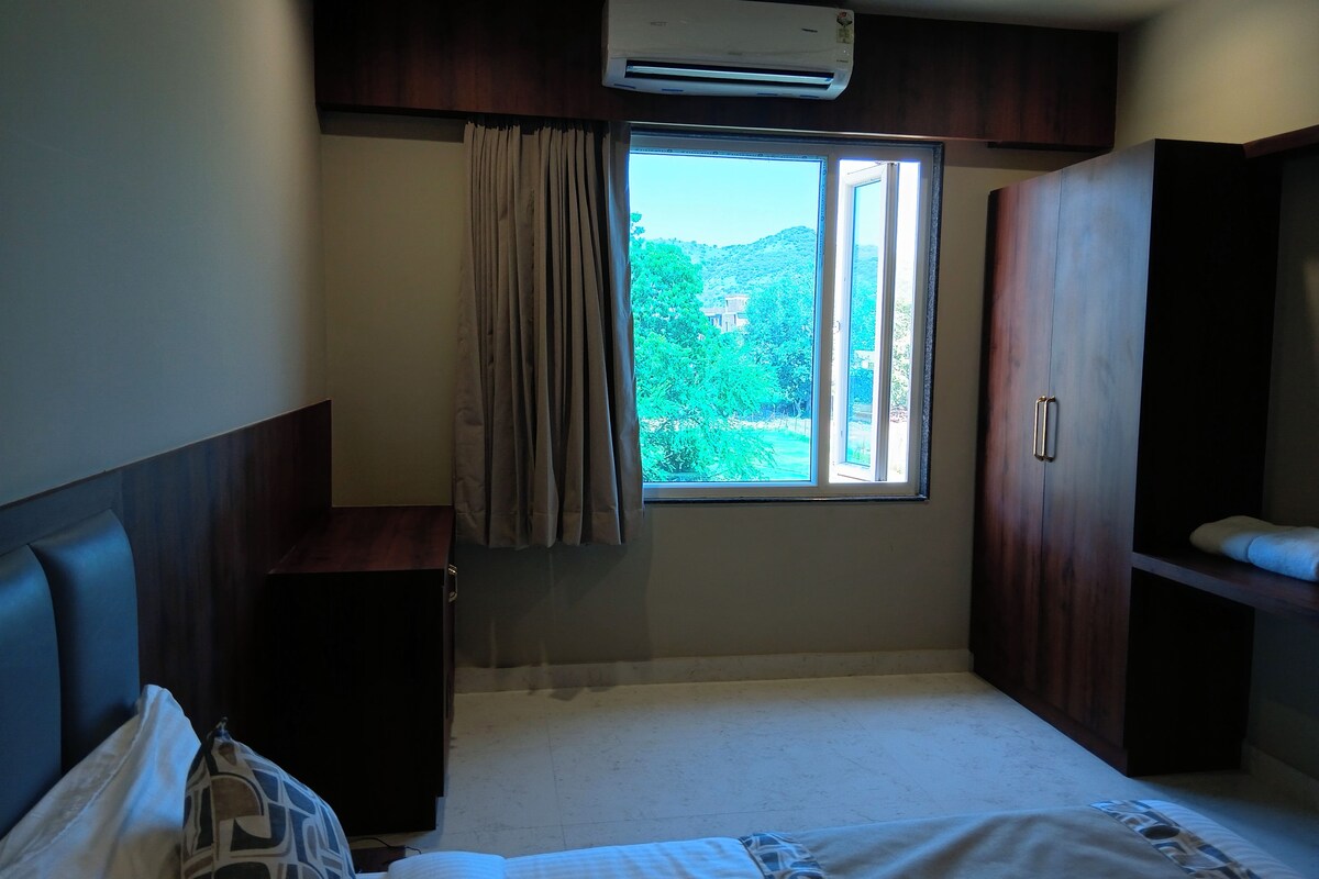 Una habitación de hotel con cama, escritorio, aire acondicionado y ventana con cortinas.