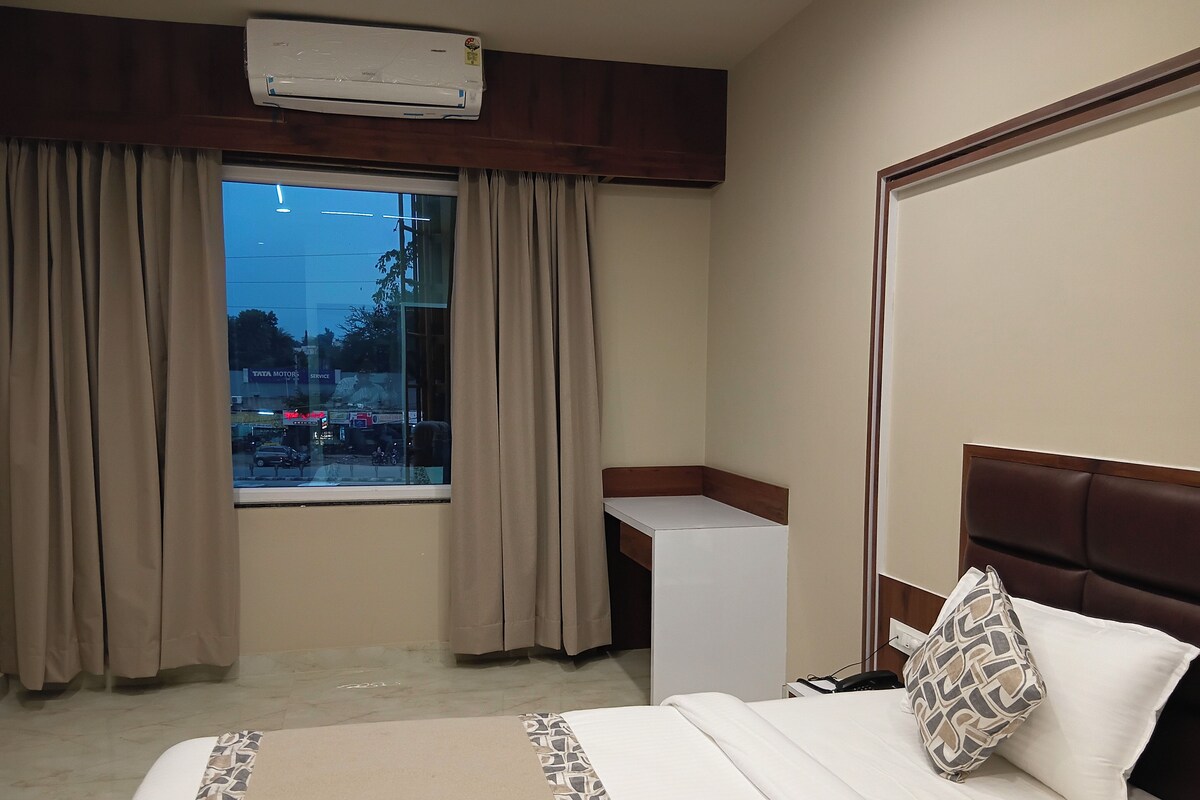 Una habitación de hotel con cama, mesita de noche, aire acondicionado y ventana con cortinas.