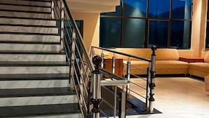 A staircase with a metal railing leading to a landing, a seating area with a sofa, and large windows with a view. - The Lalan Palace (Udaipur)