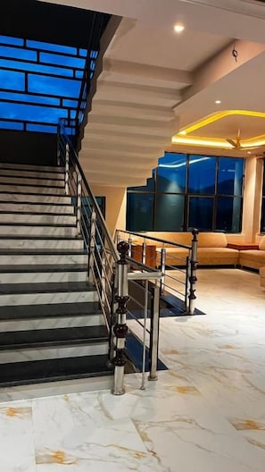 A staircase with a metal railing leading to a landing, a seating area with a sofa, and large windows with a view. - The Lalan Palace (Udaipur)
