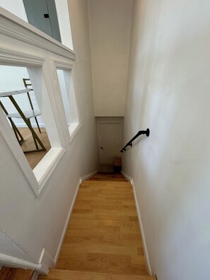 Una escalera con peldaños de madera y paredes blancas, que lleva a una puerta en la parte superior.