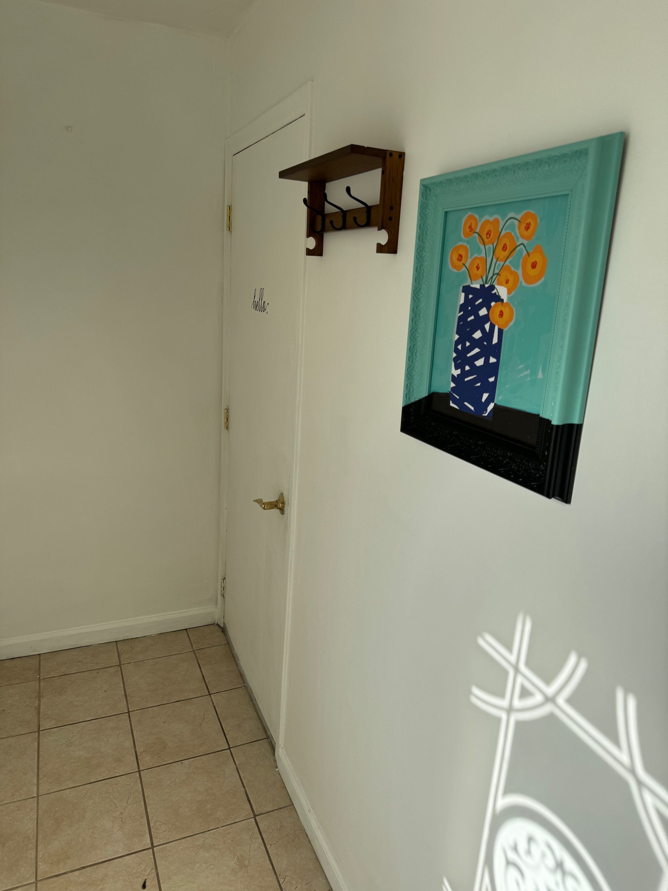 A hallway with a white door, a wall-mounted shelf with a vase of flowers, and a tiled floor.