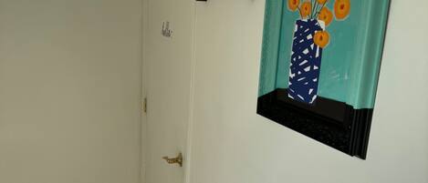 A hallway with a white door, a wall-mounted shelf with a vase of flowers, and a tiled floor.