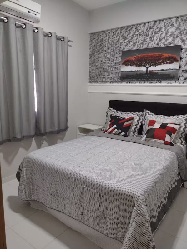Une chambre à coucher comprenant un lit, des rideaux, une table de chevet, un climatiseur fixé au mur et un papier peint à motifs au-dessus du lit.