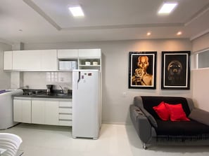Un espace de vie compact comprenant un coin cuisine, un canapé avec des coussins rouges et deux œuvres d’art encadrées accrochées au mur.