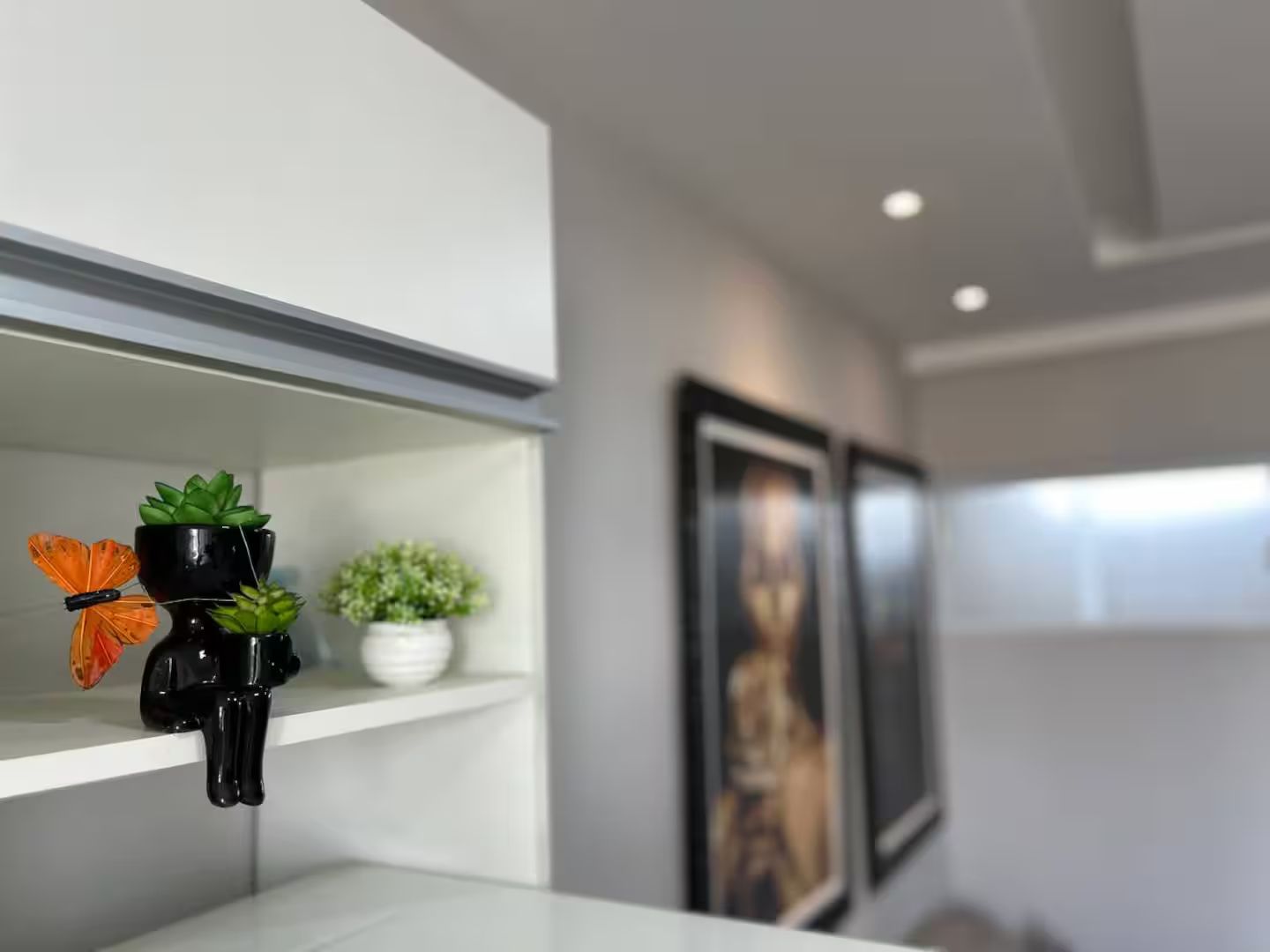 Un interior modern amb una estant blanca plena de plantes i una papallona decorativa.