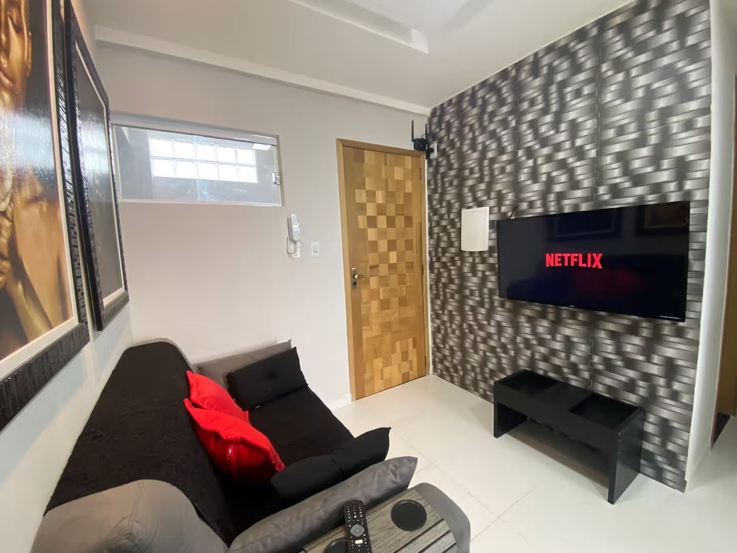 Una sala de estar moderna con un televisor de pantalla plana montado en una pared con textura, un sofá con cojines y una puerta con panel de madera.