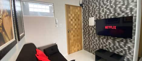 Een moderne woonkamer met een flatscreen televisie aan een gestructureerde muur, een bank met kussens en een deur met houten paneel.