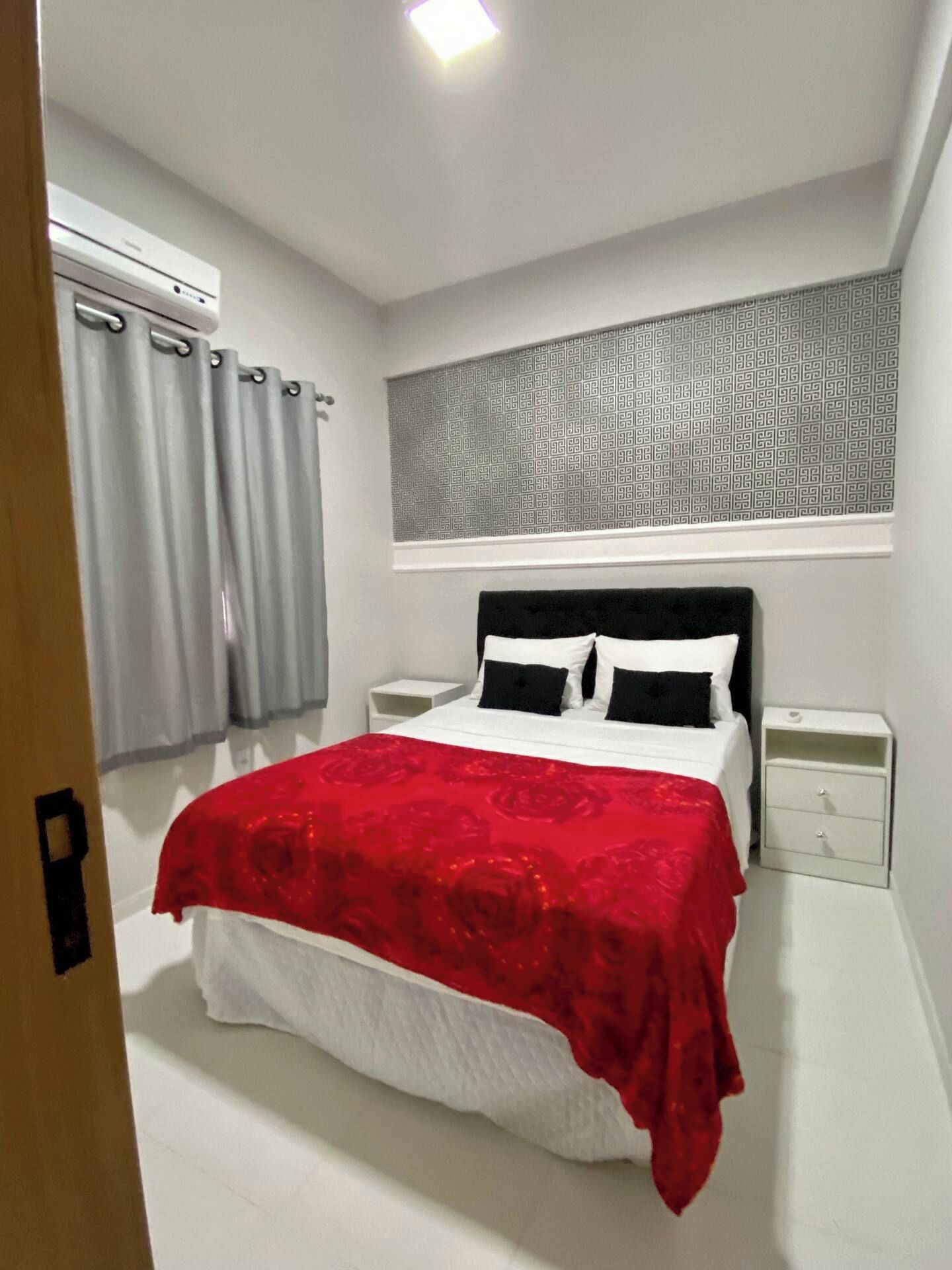Une chambre à coucher avec un lit, deux tables de chevet, une fenêtre avec des rideaux et un mur décoré d’un motif au-dessus du lit.