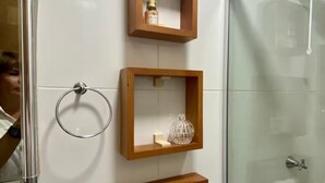 A bathroom with white tiles, a glass shower enclosure, and wooden shelves holding toiletries. - Apartment 304 · 304 2 bedrooms - Stylish and Comfortable (Belém)