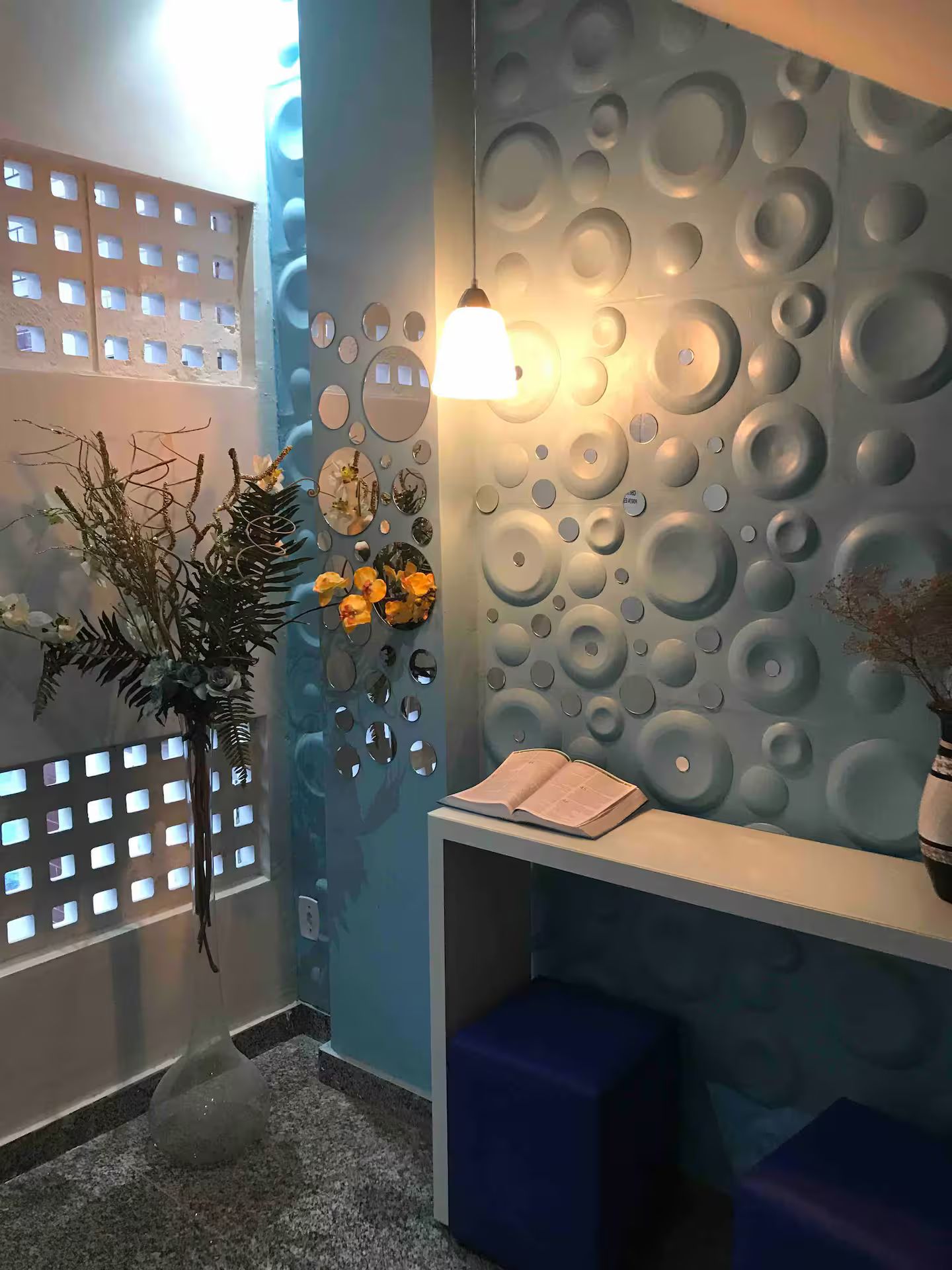 Een receptiegedeelte met een blauwe muur met cirkelvormige patronen, een receptiebalie met een lamp en een decoratieve bloemen- en begroeiingsopstelling.