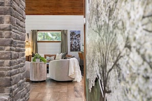 A cozy room with a stone wall, a round table, a sofa, and a large window with curtains. - Dogwood Dusk · New! Romantic Getaway – Hot Tub & Fireplace (Broken Bow)