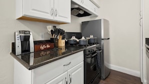 A kitchen with white cabinets, a coffee maker, a stove, pots, and a refrigerator. - The Loop Loft | Stylish Stay Near Q2 Stadium (Austin)