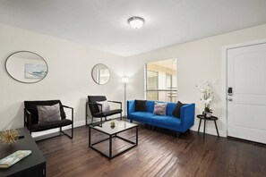 A living room with a blue sofa, two black chairs, a coffee table, and a round mirror on the wall.