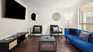 A modern living room with a flat-screen TV, two armchairs, a blue sofa, a coffee table, and a floor lamp. - The Loop Loft | Stylish Stay Near Q2 Stadium (Austin)
