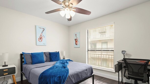 A bedroom with a bed, a desk, a chair, a ceiling fan, and two wall-mounted artworks. - The Loop Loft | Stylish Stay Near Q2 Stadium (Austin)