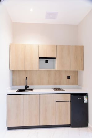 A modern kitchen with light wood cabinets, a black dishwasher, and a stainless steel sink. - Olana Hotel (Riyadh)