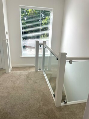 A room with a carpeted floor, a window with blinds, and a glass railing. - Brand New detached 3 bedroom 2 bathroom house on the edge of Epping Forest (Coopersale)
