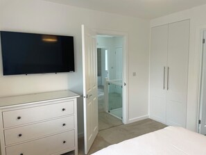 A bedroom with a bed, a dresser, a television, and a closet. - Brand New detached 3 bedroom 2 bathroom house on the edge of Epping Forest (Coopersale)
