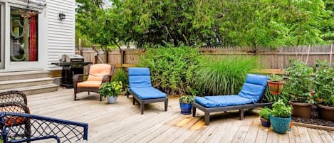 En træterrasse med udendørs møbler, grill og krukker med planter.