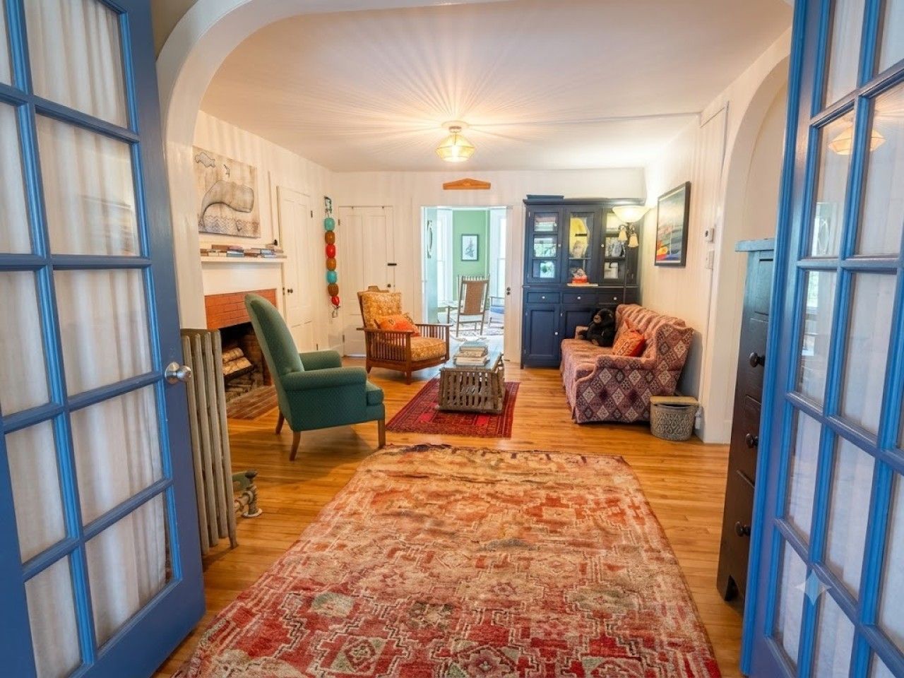 A spacious living room with a large rug, a green armchair, and a patterned sofa.