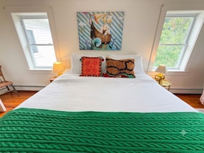 Un dormitorio con una cama grande, dos ventanas, un cuadro en la pared y una manta verde.