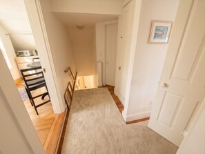 A hallway with a carpet, wooden flooring, a black chair, a white door, and a framed picture on the wall.