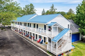 A two-story motel with a blue roof, a covered front porch with red and blue chairs, and a small garage.