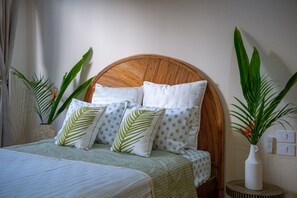 Ein Bett mit einem gewobenen Kopfteil, mehreren Kissen und einer grünen Bettdecke.