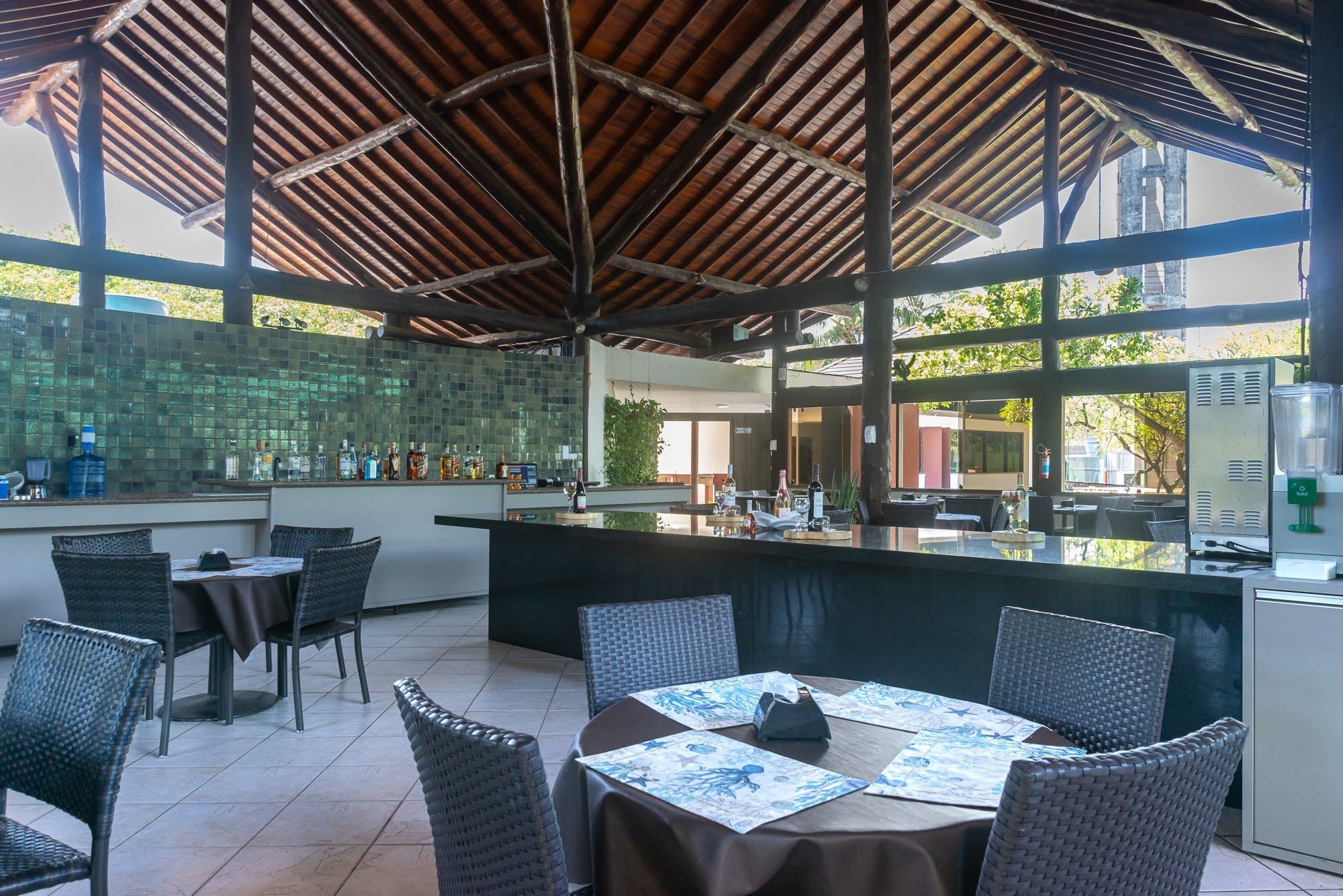 Un restaurant en plein air doté d’un espace repas couvert, d’un bar et offrant une vue sur la verdure environnante.