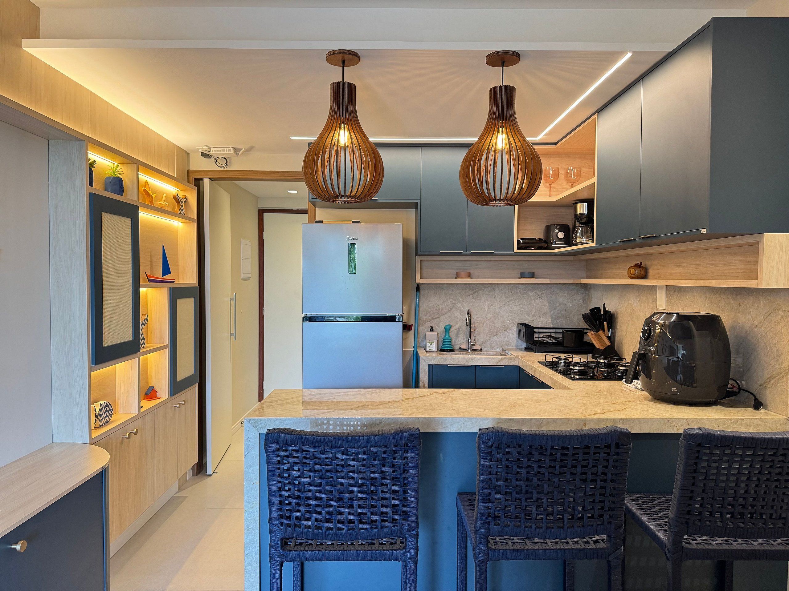 A modern kitchen with a central island, two hanging pendant lights, and a built-in refrigerator.