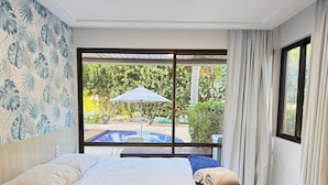 A hotel room with a bed, a view of a swimming pool, and a large window with curtains. - Nannai Residence Muro Alto Beira Mar (N. Sra. do Ó)