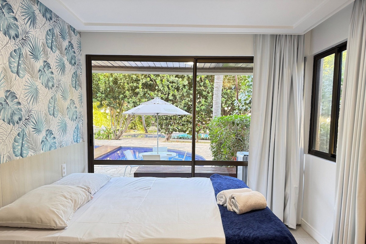 A hotel room with a bed, a view of a swimming pool, and a large window with curtains.