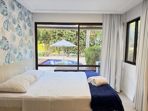A hotel room with a bed, a view of a swimming pool, and a large window with curtains. - Nannai Residence Muro Alto Beira Mar (N. Sra. do Ó)
