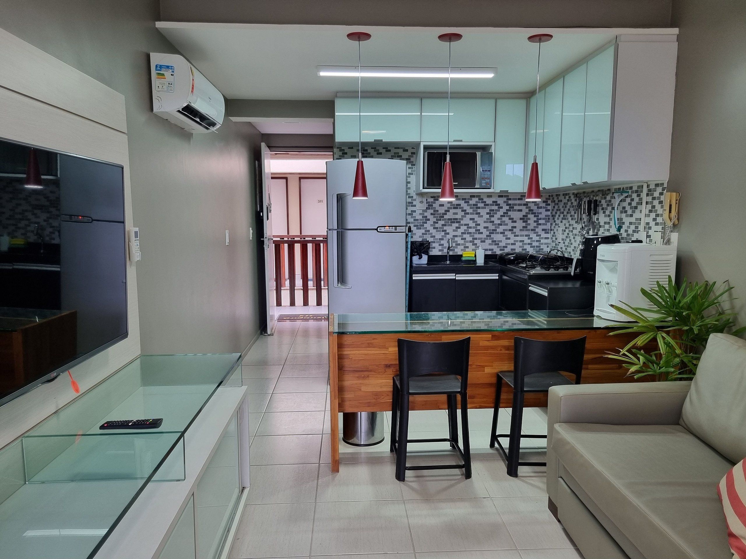 A modern kitchen with a glass island, black chairs, and a beige sofa.