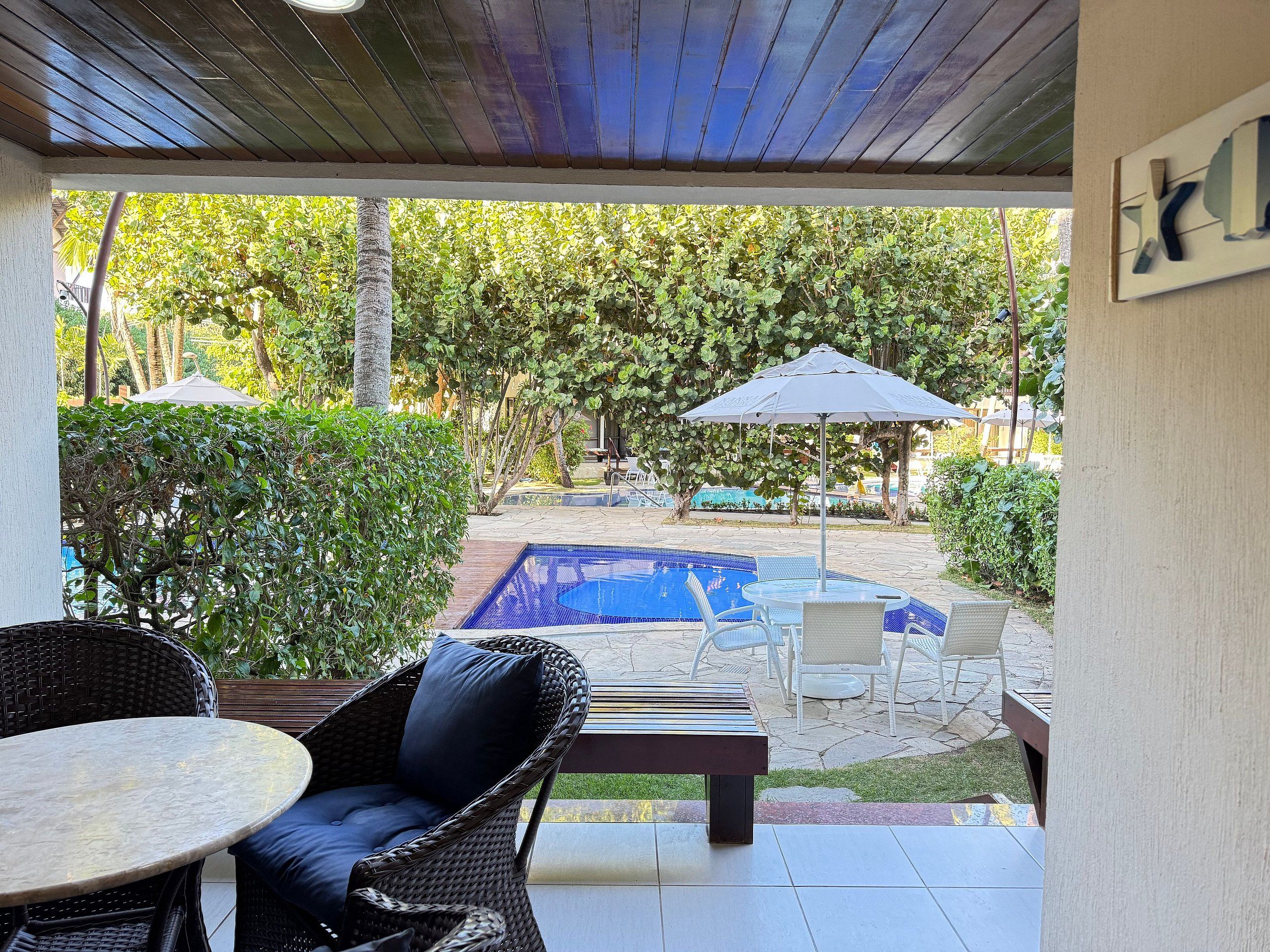 Een overdekt terras met een zwembad, tuinmeubilair en uitzicht op de achtertuin.