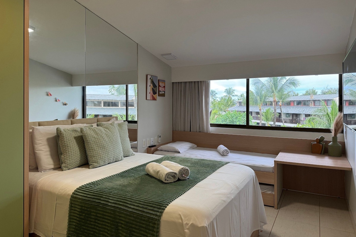 A hotel room with a bed, a desk, a large window, and a view of the outside.