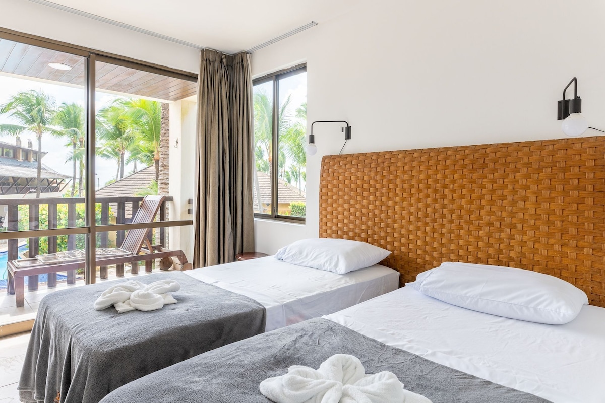 A hotel room with two beds, a balcony with a view of palm trees, and a woven headboard.
