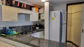 Une cuisine dotée d’un plan de travail en granit, de meubles blancs, d’une cuisinière et d’un réfrigérateur.