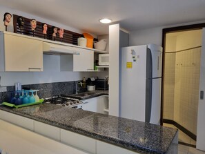 A kitchen with a granite countertop, white cabinets, a stove, and a refrigerator. - Nannai Residence Muro Alto Beira Mar (N. Sra. do Ó)