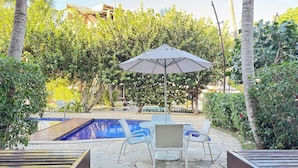 A pool area with a lounge chair and umbrella, surrounded by lush greenery and a clear blue pool. - Nannai Residence Muro Alto Beira Mar (N. Sra. do Ó)