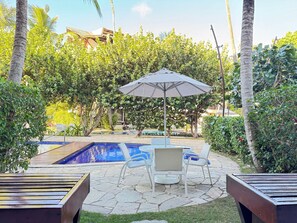 A pool area with a lounge chair and umbrella, surrounded by lush greenery and a clear blue pool. - Nannai Residence Muro Alto Beira Mar (N. Sra. do Ó)